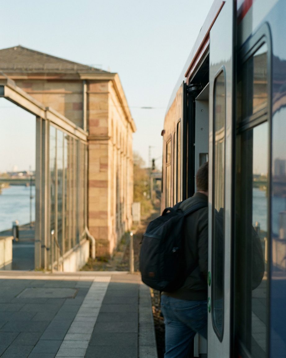 Offene Regionalzug-Tür, ein einsteigender Fahrgast mit Rucksack von hinten, Hochformat.