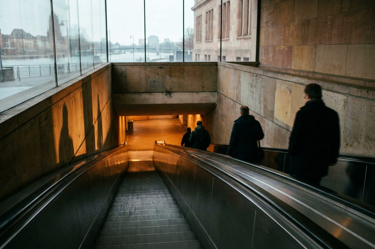 Eine abwärts führende Rolltreppe im warmen Kunstlicht, Metallwände werfen harte Schatten.