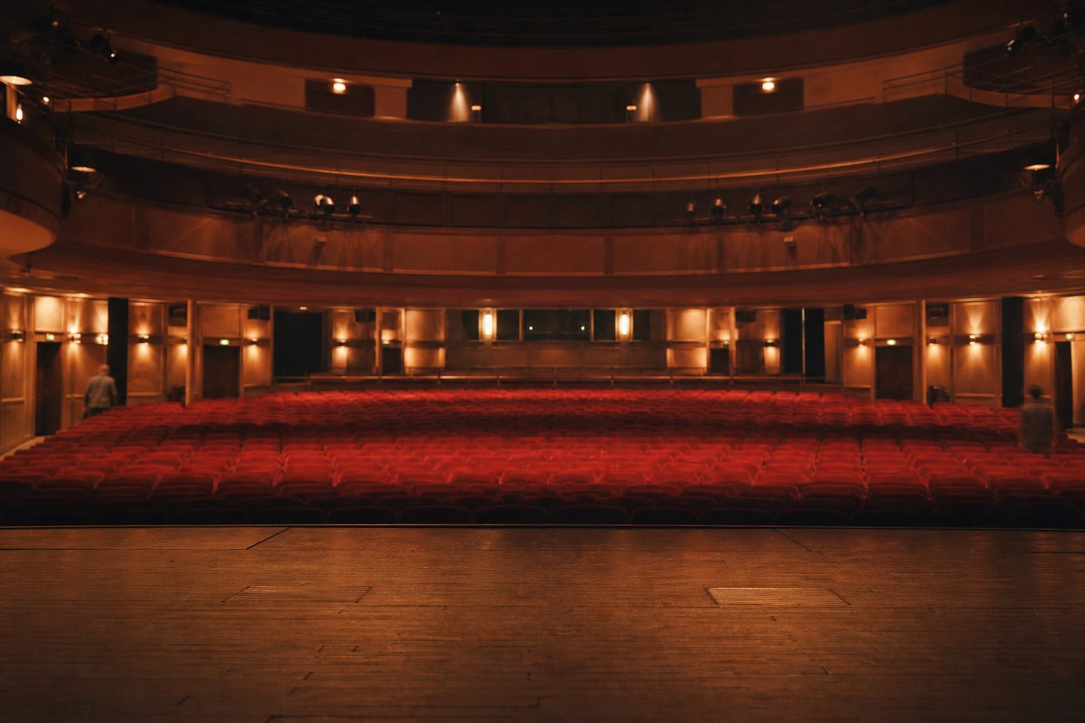 Der leere Theatersaal mit roten Sitzreihen im warmen Bühnenlicht, fotografiert von der Bühne aus.