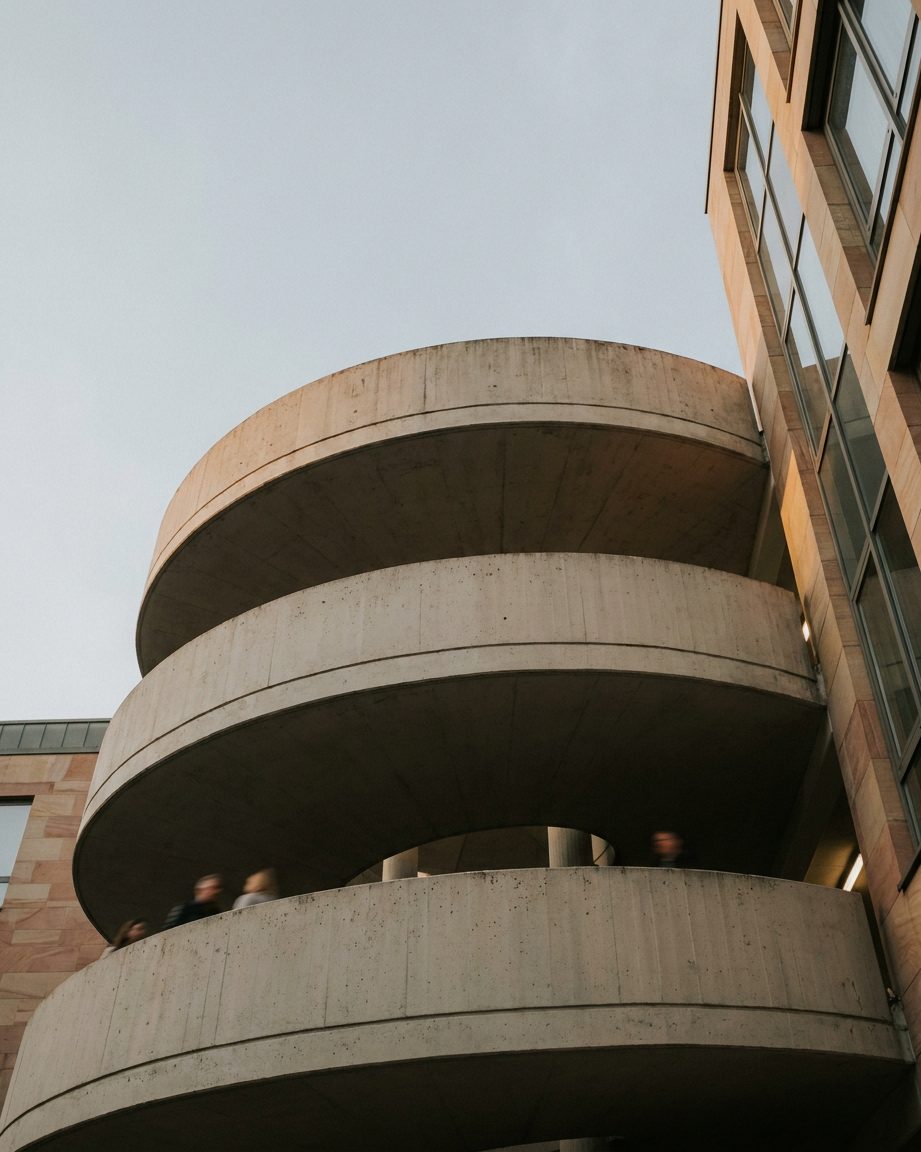 Wendelrampe eines Parkhauses von unten fotografiert, die Betonspirale windet sich gegen den Himmel.