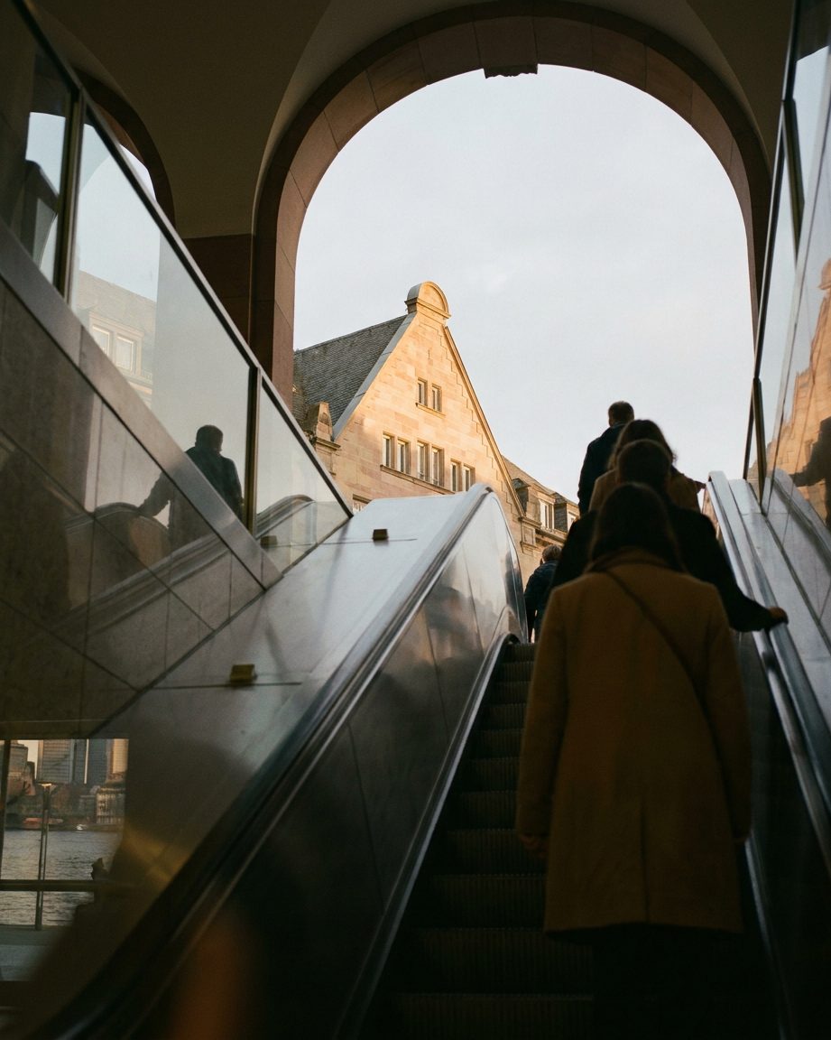 Blick eine Rolltreppe der B-Ebene hinauf, oben im Gegenlicht der Sandsteingiebel der Hauptwache gegen den Himmel.