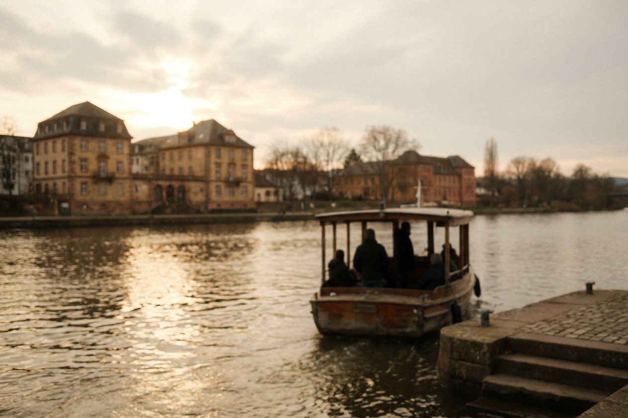 Die kleine Mainfähre legt am Höchster Ufer an, Fahrgäste als Silhouetten gegen das glitzernde Wasser.