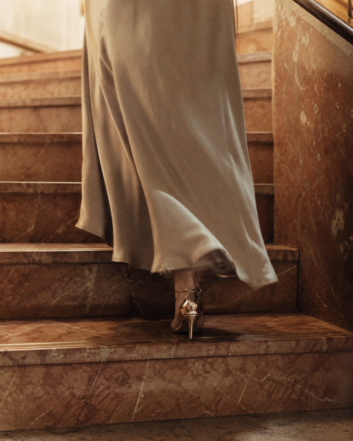 Eine Marmortreppe mit dem Saum eines Abendkleids und glänzenden Schuhen, hochformatig, keine Gesichter.