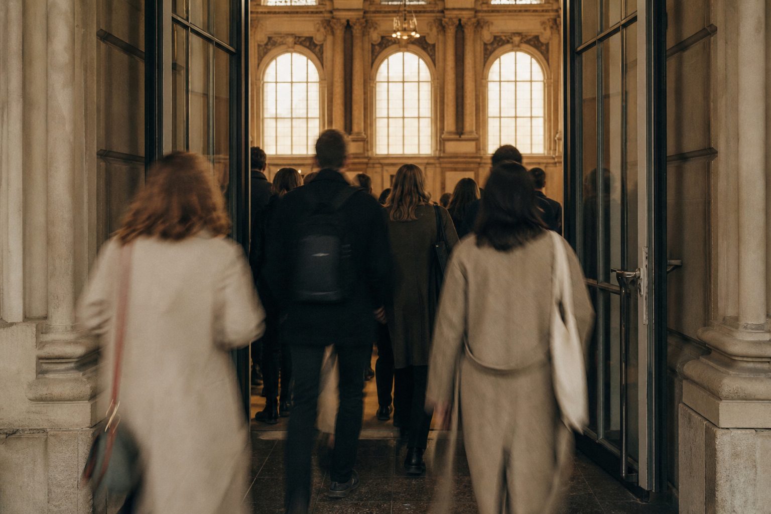 Menschen von hinten, die beim Pausengong durch hohe Flügeltüren zurück in den Zuschauersaal strömen.
