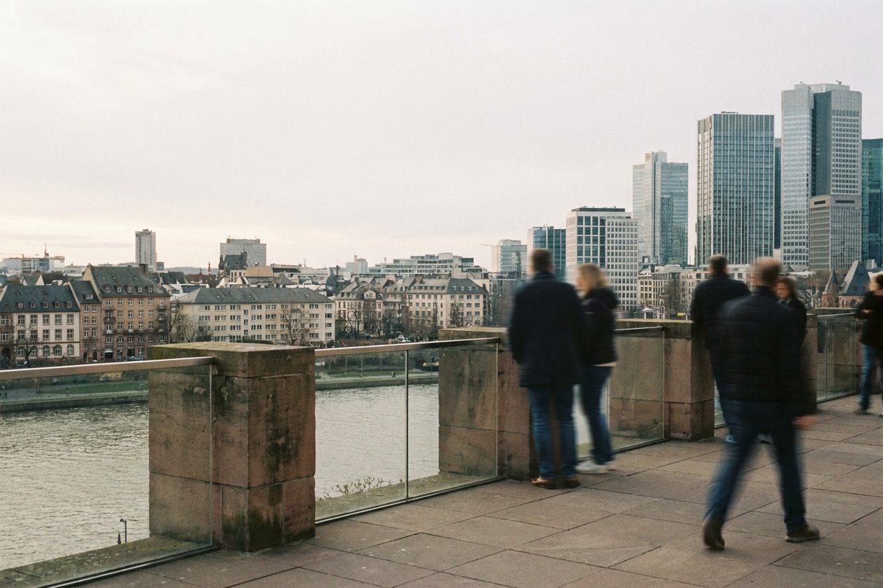 Besucher stehen als Rückenfiguren an der Brüstung der Aussichtsplattform, vor ihnen das Häusermeer der Frankfurter Innenstadt.