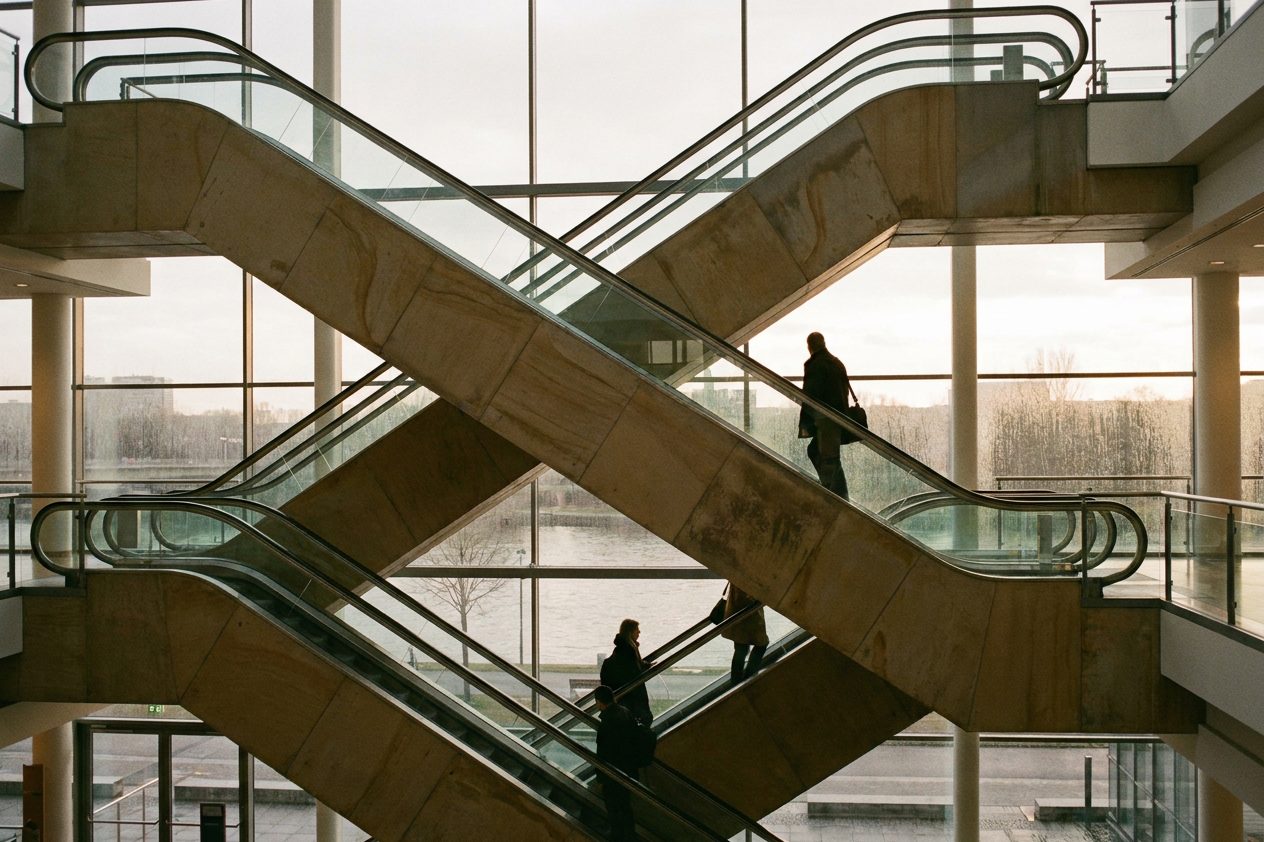 Übereinanderliegende Rolltreppen in einem Eingangsbauwerk der Messe, Besucher mit Taschen von hinten.