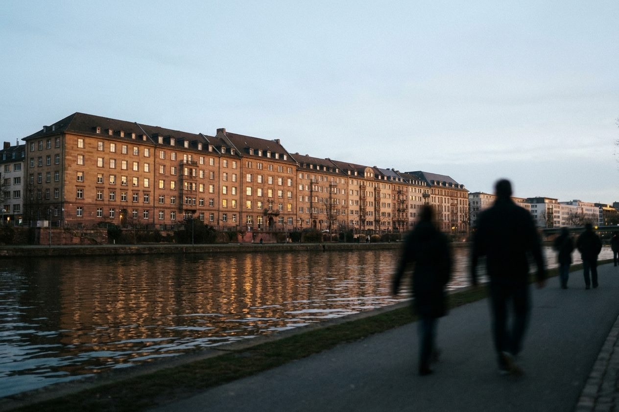 Abendlich erleuchtete Wohnungsfenster einer langen Wohnhausfassade zur blauen Stunde.