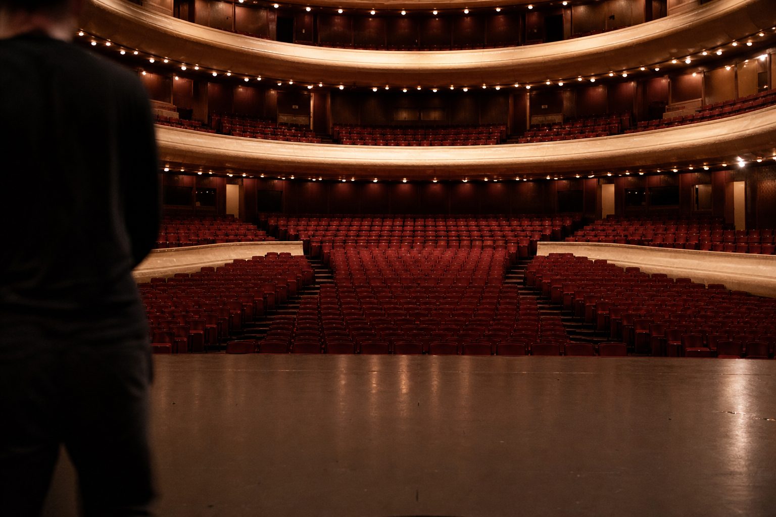 Blick von der Bühnenkante in den leeren, dunkelrot ausgekleideten Zuschauersaal der Oper Frankfurt mit beleuchteten Rängen.