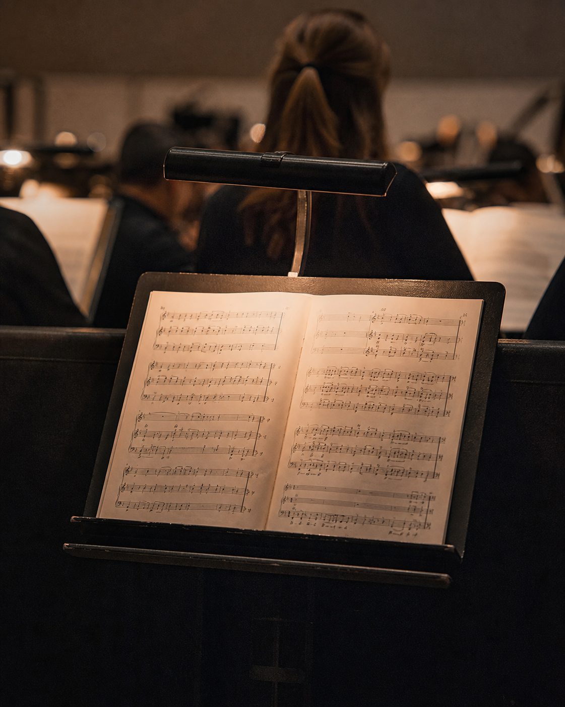 Ein Notenpult mit aufgeschlagener Partitur im Orchestergraben, warm beleuchtet vom Pultlicht, hochformatig fotografiert.