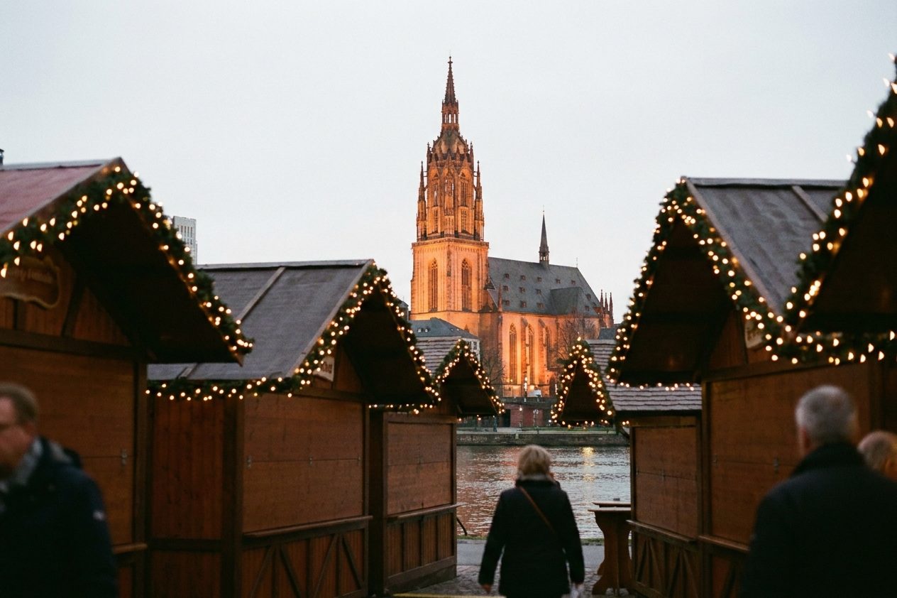Blick über die beleuchteten Budendächer mit Lichterketten hinweg zum angestrahlten gotischen Turm des Frankfurter Kaiserdoms.